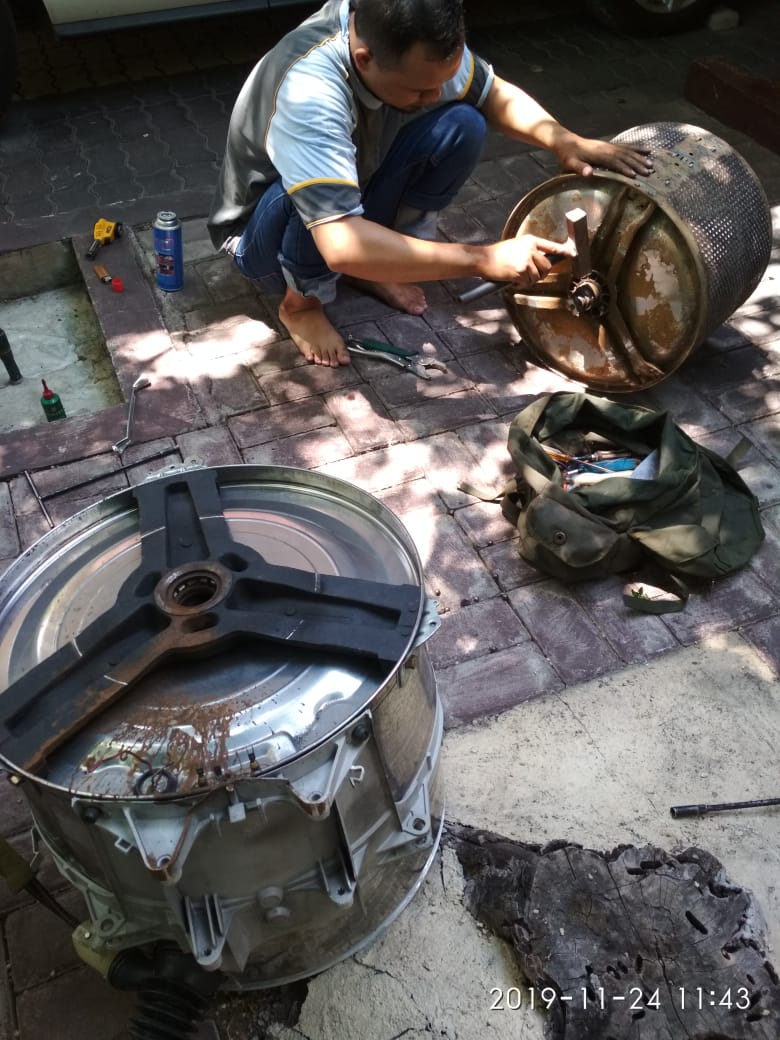 Close-up view of a technician's hands disassembling a washing machine drum with precision tools, showcasing professional repair work in a clean workshop environment