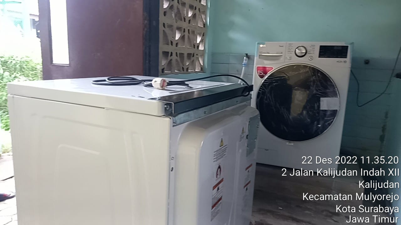 Team of technicians installing a new washing machine unit with hoses and electrical connections in a residential kitchen